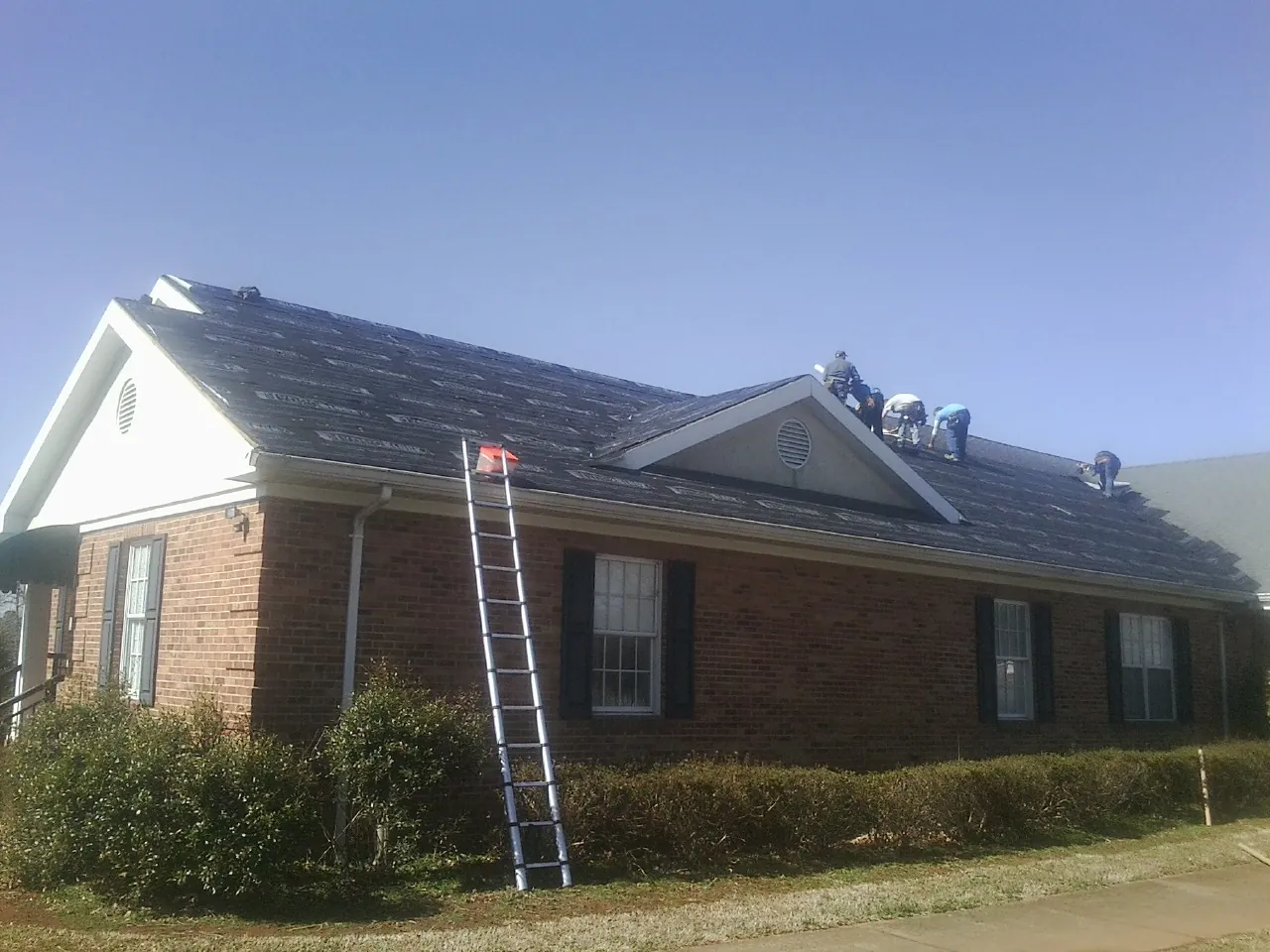 Crew tearing shingles off a brick ranch roof with a ladder set — Metal Roof Repair work by our crew in Water View