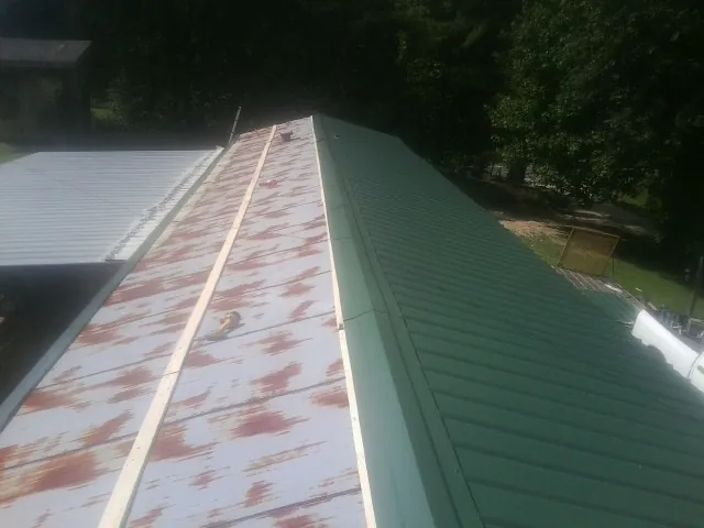 Old rusted panels beside newly installed green metal roofing — Wind Damage Roof Repair by Roofing Brothers in Water View