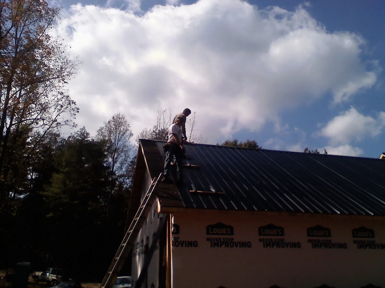 Roofer fastening dark metal panels high against a cloudy sky, from a Roof Inspection job in Water View