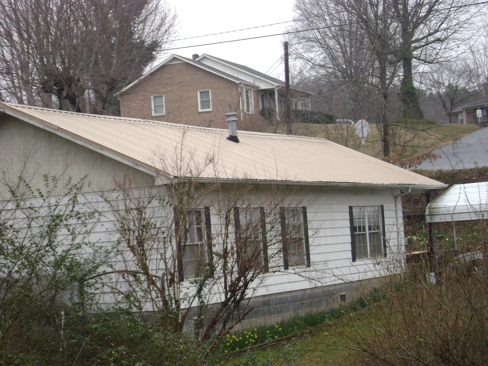 Tan metal roof on a white sided house set into a hillside — Commercial Roofing by Roofing Brothers in Water View