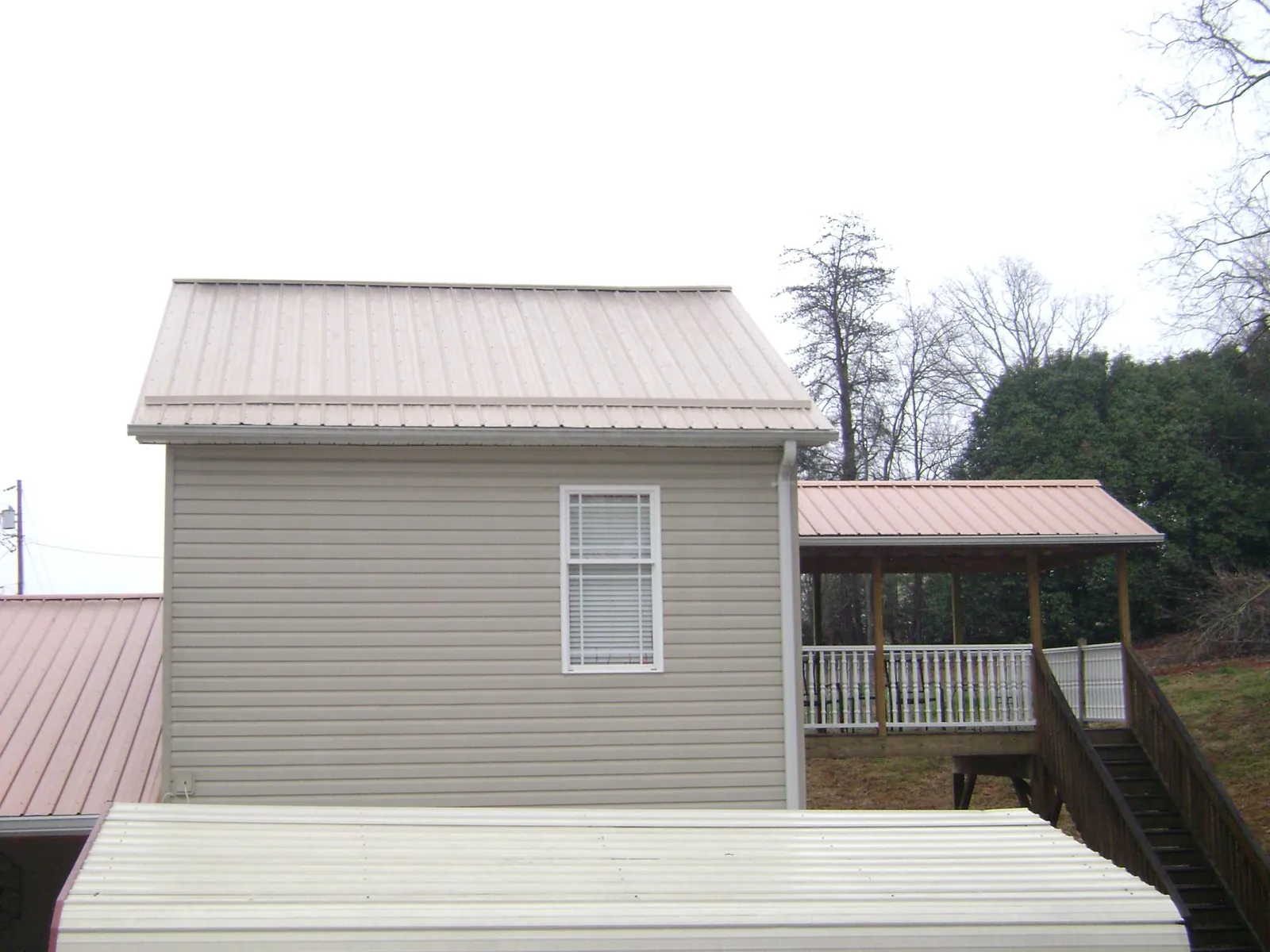 Tan metal roofs on a two story addition and attached porch, from a Roof Replacement job in Water View